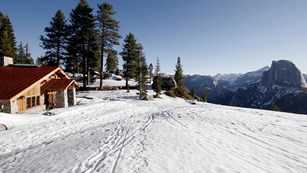 A wooden ski hut looks out over snow-covered Glacier Point, with Half Dome.