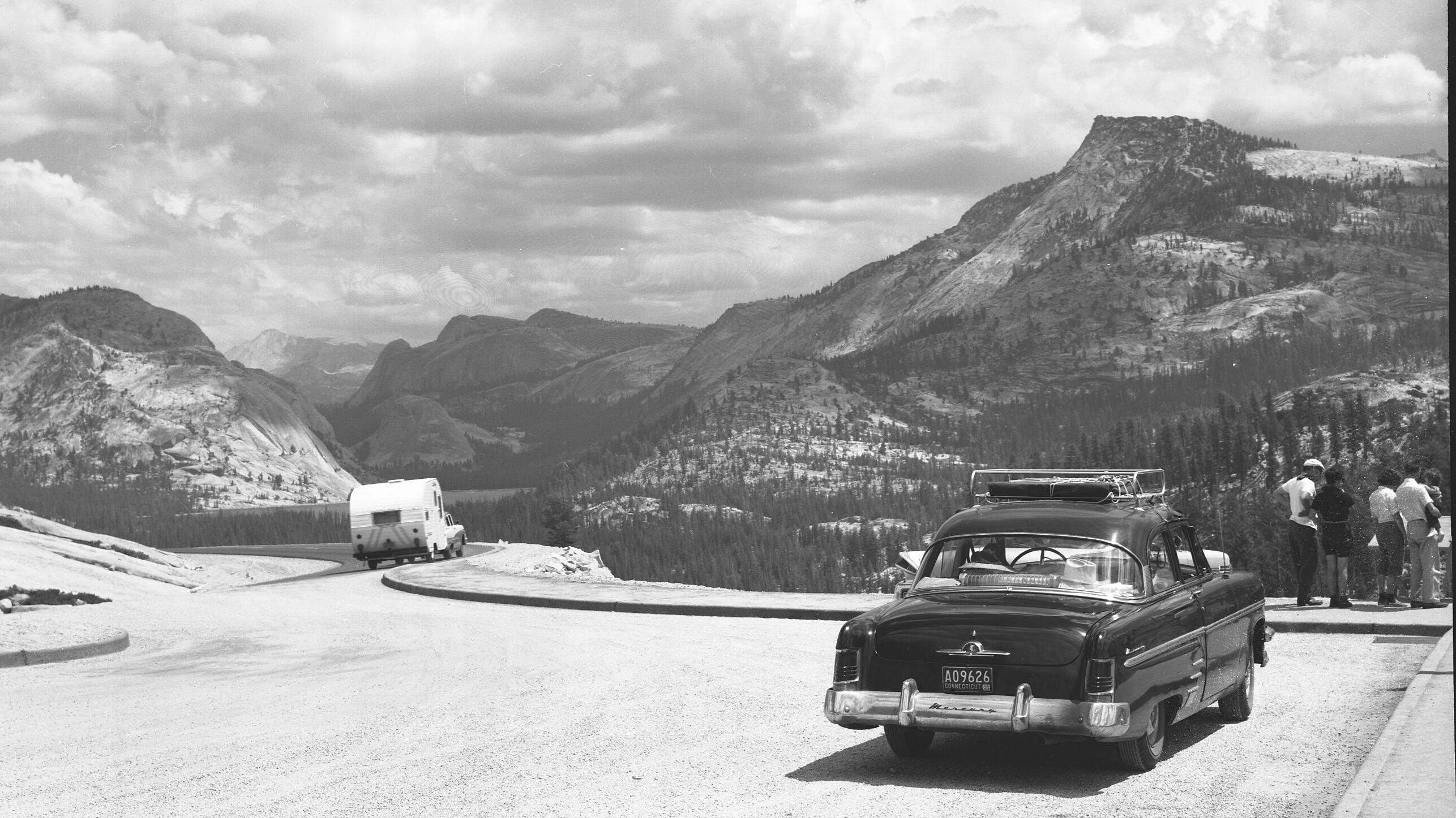 A paved pull-out area alongside a road with a car parked and mountains in the distance