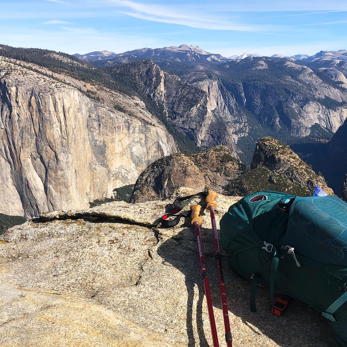 A backpack and trekking poles sit on a granite ledge overlooking Yosemite Valley