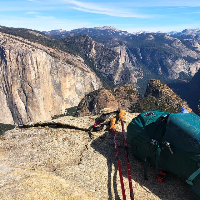A backpack and trekking poles sit on a granite ledge overlooking Yosemite Valley