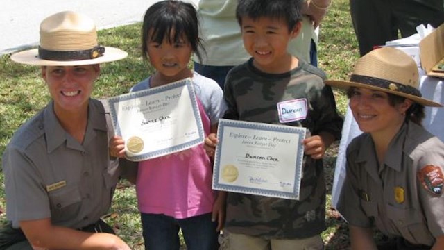 Two young individuals holding up a certificate with park rangers in their uniforms smiling