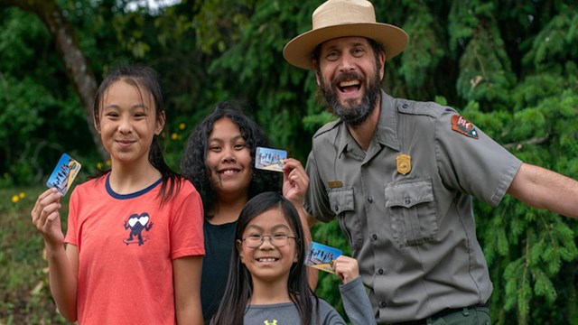 Three youth holding up passes with a park ranger