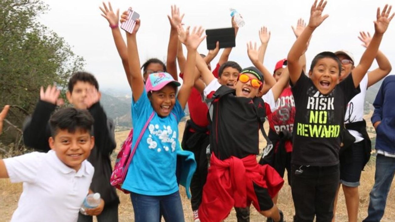 A group of happy children standing outside with their arms in the air