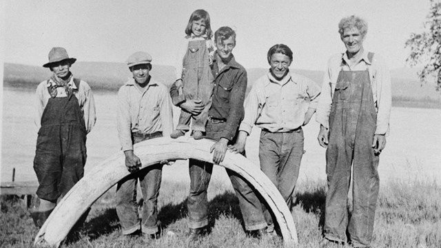 Historic photo of men standing on Yukon River shore with mammoth tusk