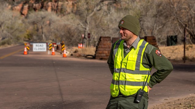 A park ranger with a high-visibility vest and black radio stands at an intersection.