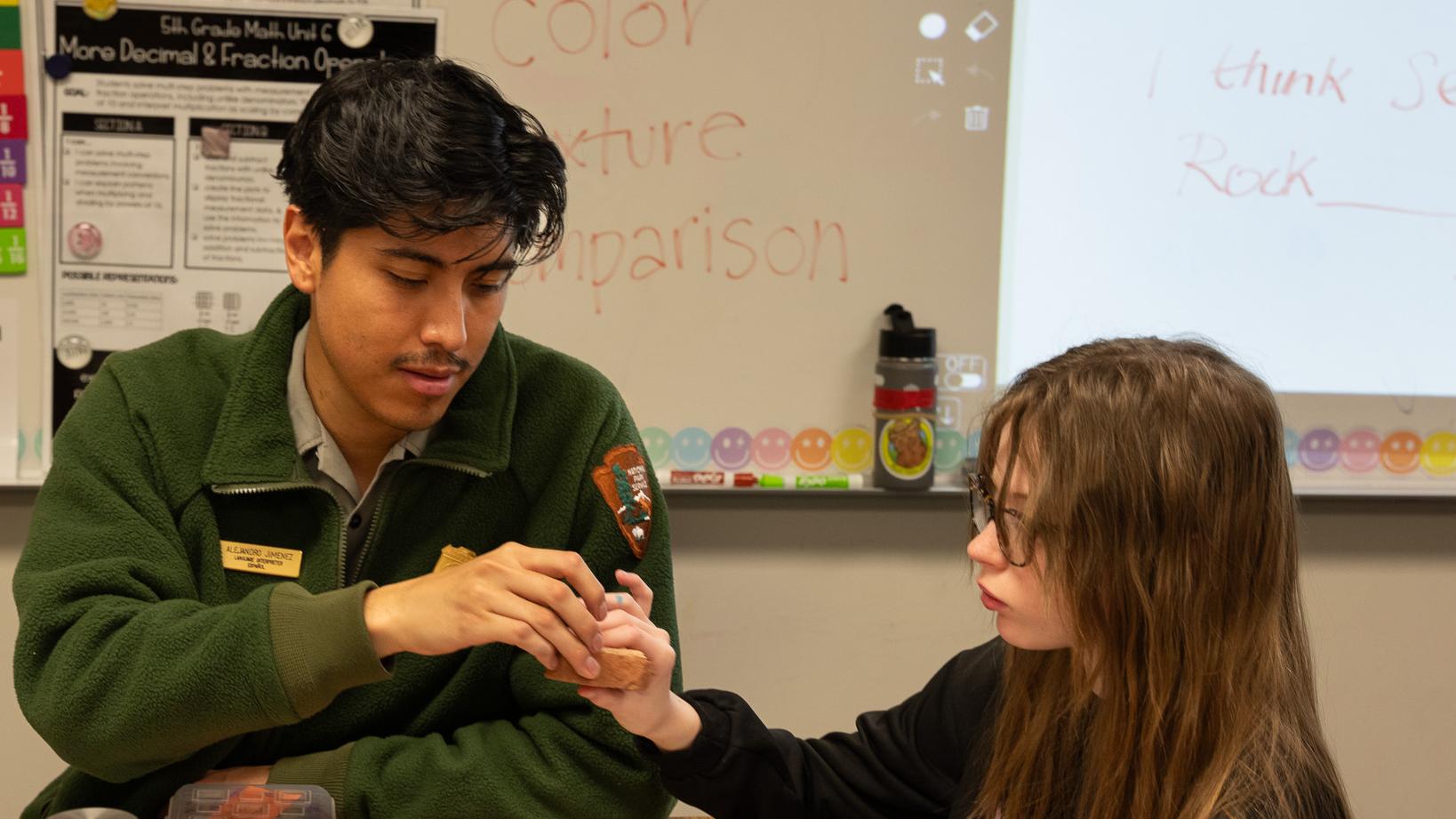 A ranger hands a piece of sandstone to a student in a classroom.