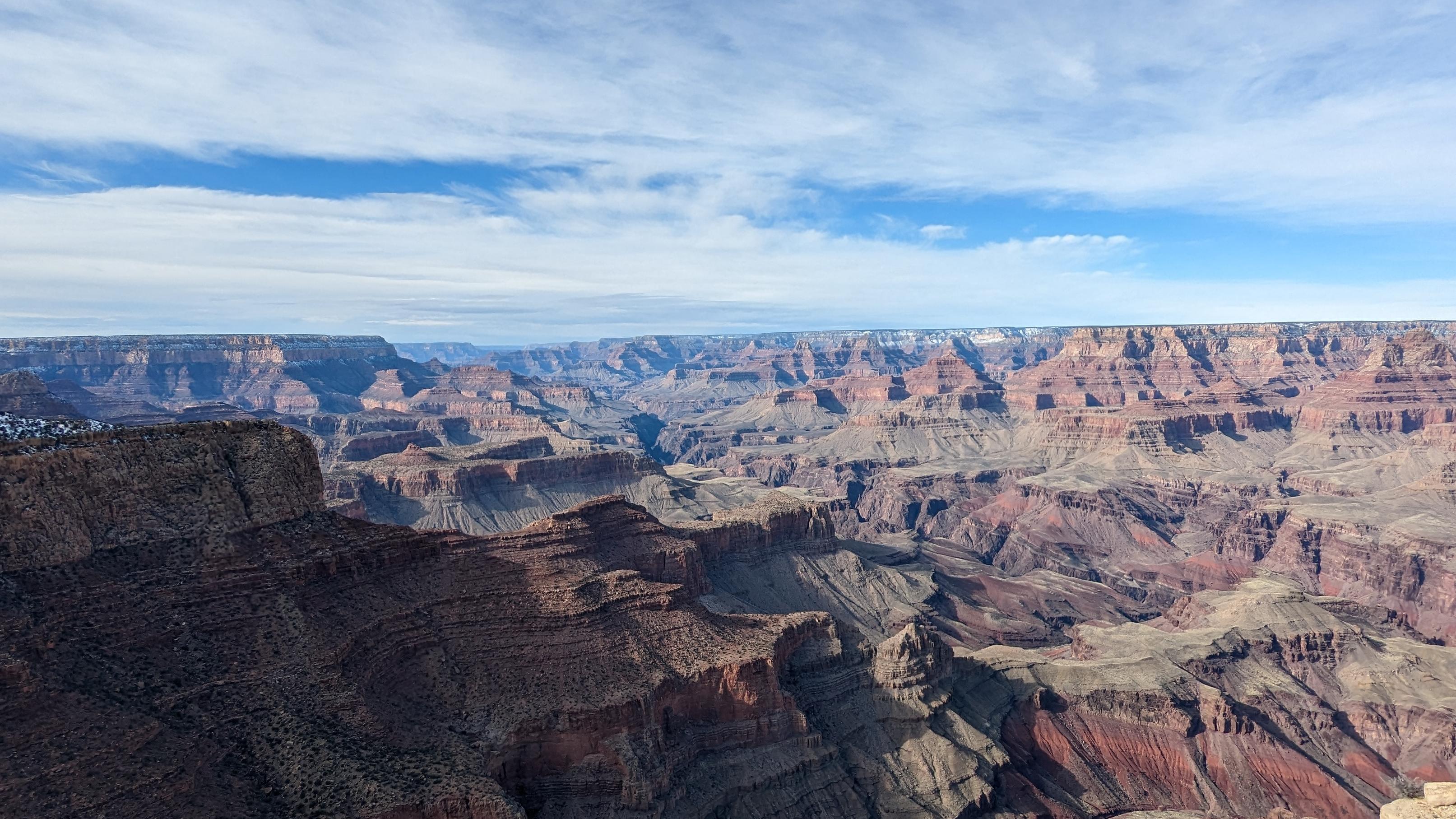 A deep canyon lined with multi-colored rocks and blue sky with clouds above.