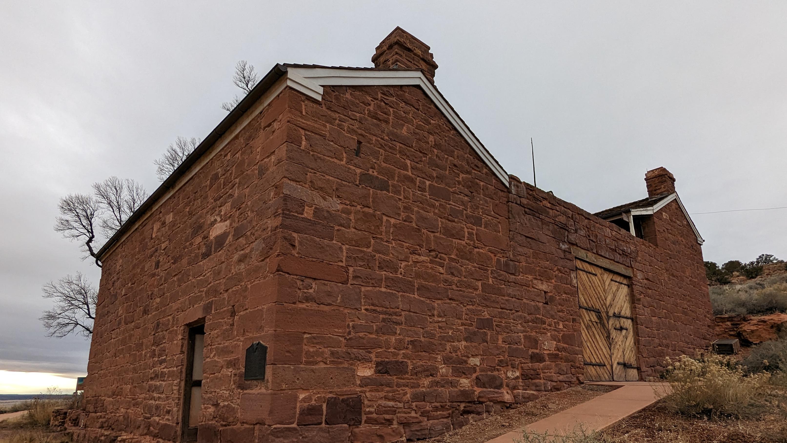 A sandstone building stands before a gray sky. The building is a fort with gates and small windows.