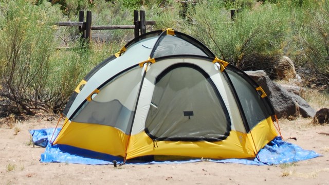 A tent in a gravel campsite. A large sandstone peak stands in the background.