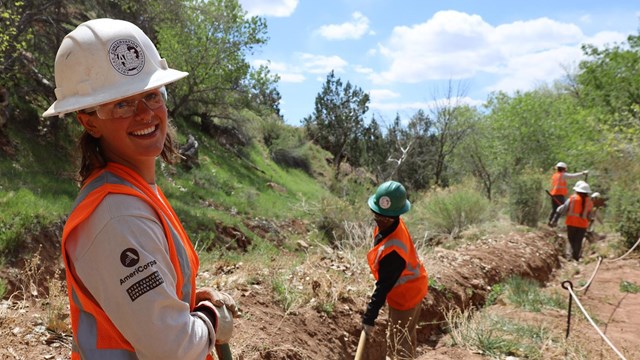 American Conservation Experience intern stands with shovel in historic irrigation ditch.