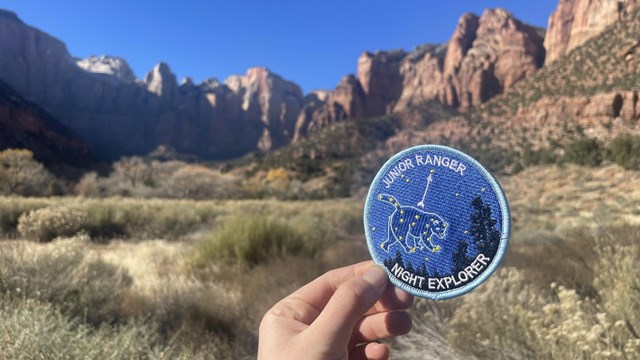 A night sky junior ranger patch, with red cliffs in the background.