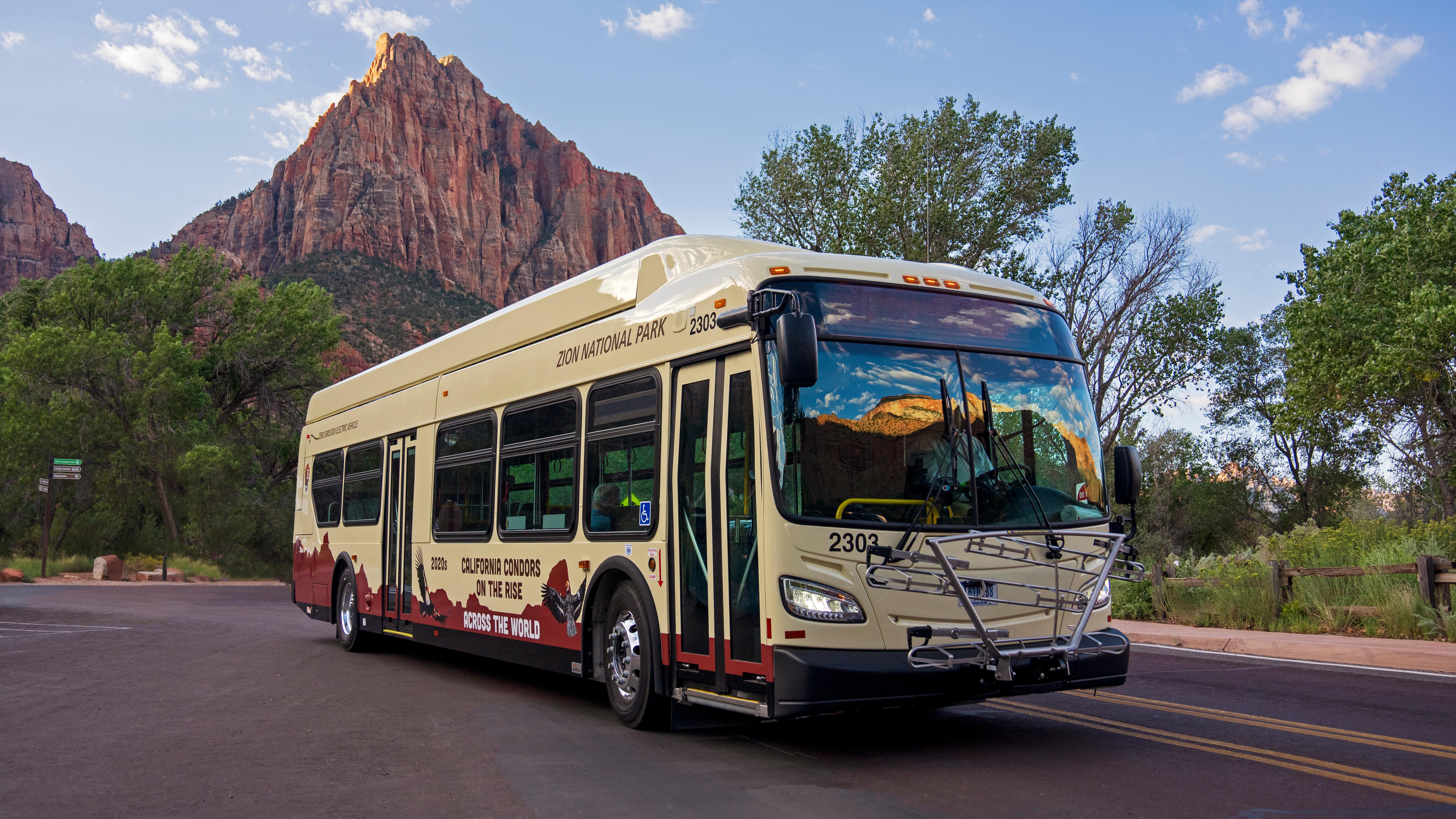 A Zion Canyon shuttle on a red road, with red sandstone formations in the background.