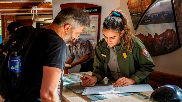 A ranger hands a visitor a map and newspaper about Zion National Park