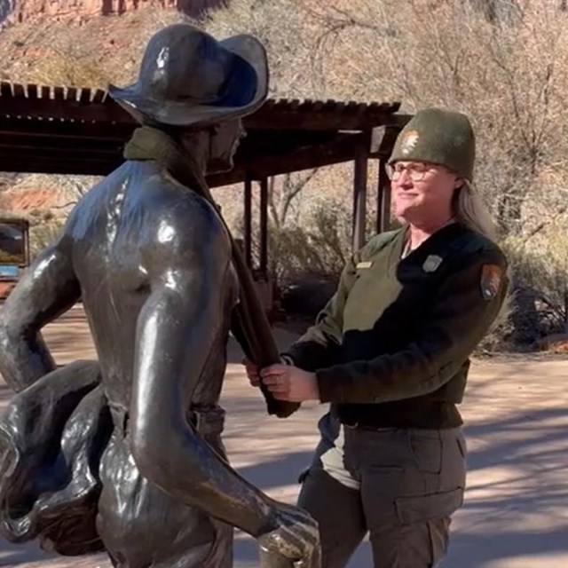 A ranger in a green uniform wraps a green scarf around the neck of a metal statue.