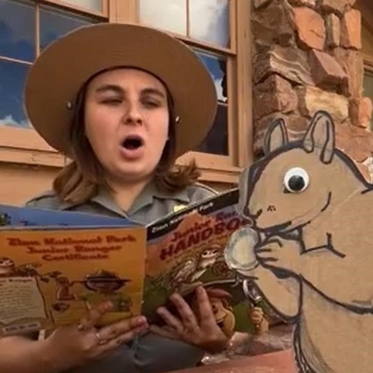 A ranger reads off a Junior Ranger book next to a cardboard cutout of a squirrel.