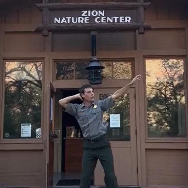 A ranger strikes a dance pose on the front steps of a stone Nature Center building.