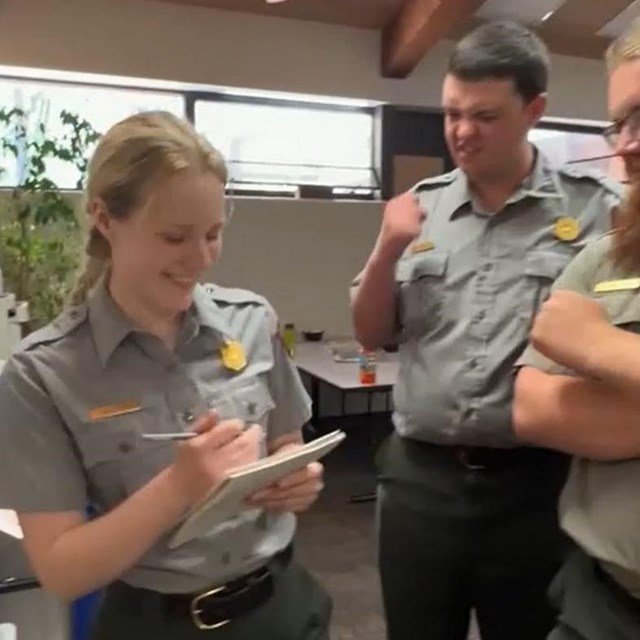 Three rangers congregate in an office. One takes notes while the other two nod in approval.