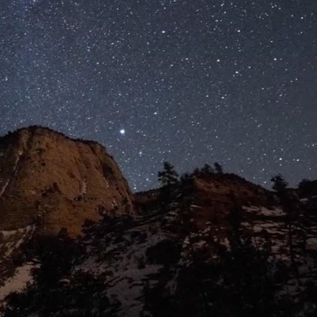 Millions of bright stars illuminate the face of a rock cliff at night.