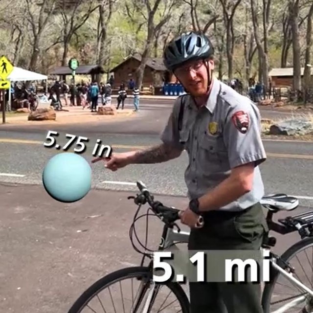 A ranger on a bike stops at The Grotto. A graphic of the blue planet of Uranus hovers on the screen.