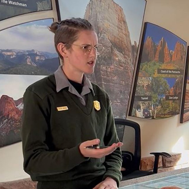 A ranger at a desk talking to a visitor with pictures of cliffs and canyons in the background