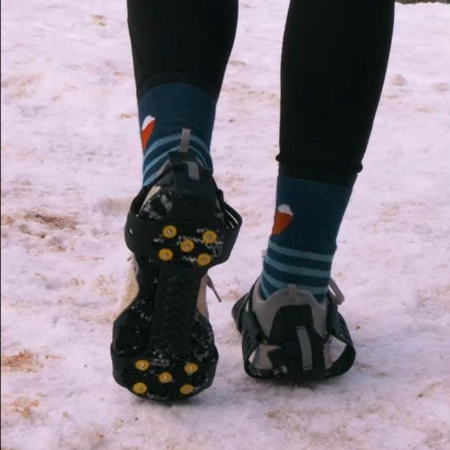 A hiker shows off their microspikes attached to their boots while standing in compacted snow.