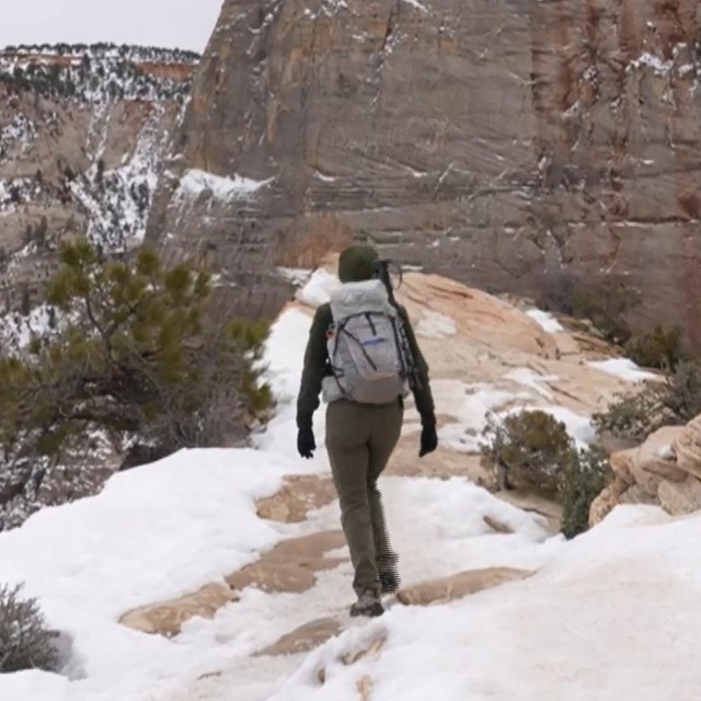 A ranger walks away from the camera along the snowy and icy summit of Angels Landing.