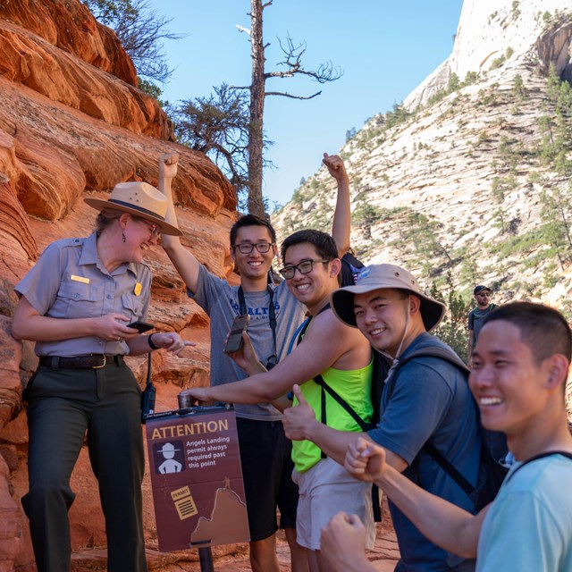 A ranger looks at a phone as a group of men smile next to orange sandstone