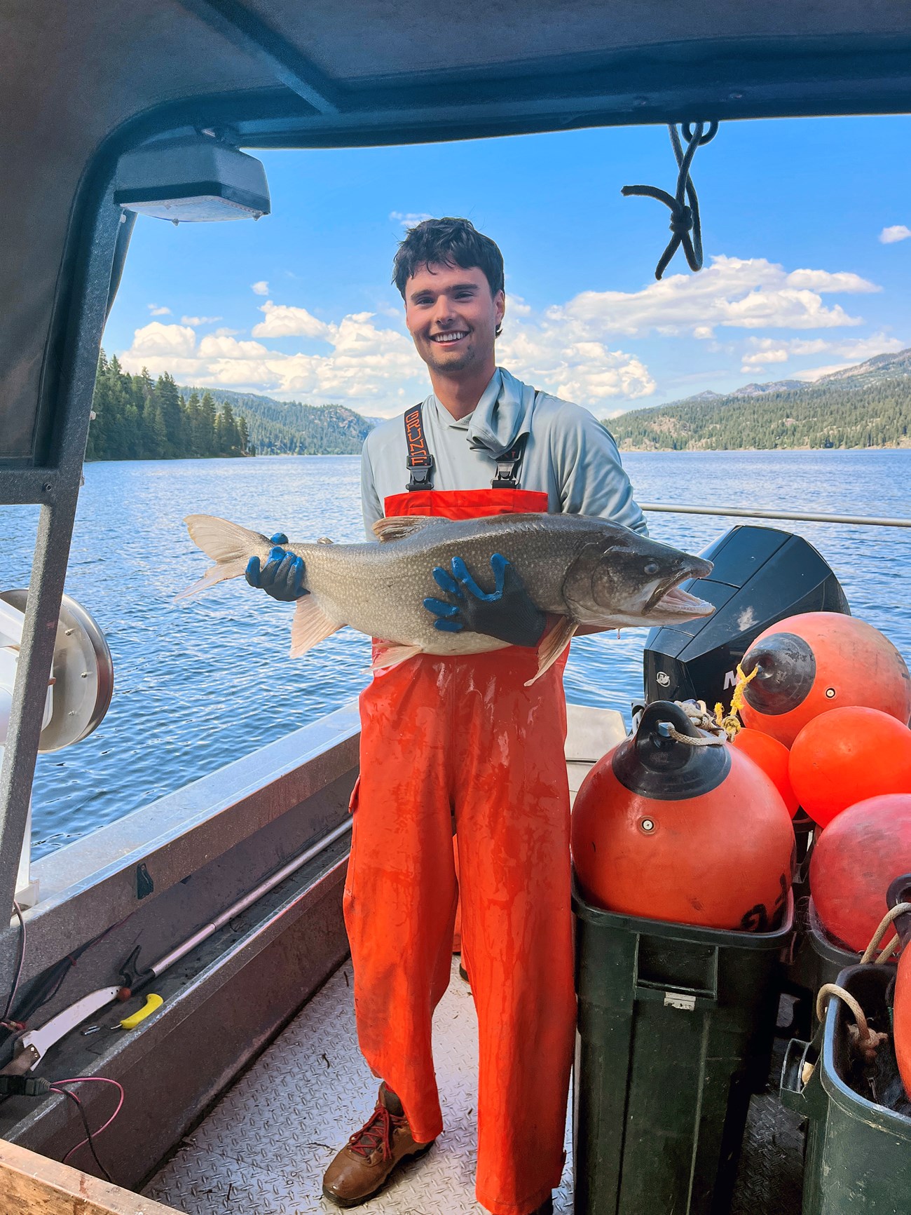 Shell on a boat in bright orange waders, smiling, holding a huge fish with both hands.