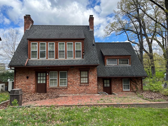 two story brick house with two chimneys, two doors, and a row of six windows on the second floor