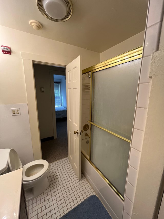 View from a small bathroom looking towards the hallway, showing tub/shower combo, toilet, and edge of sink.