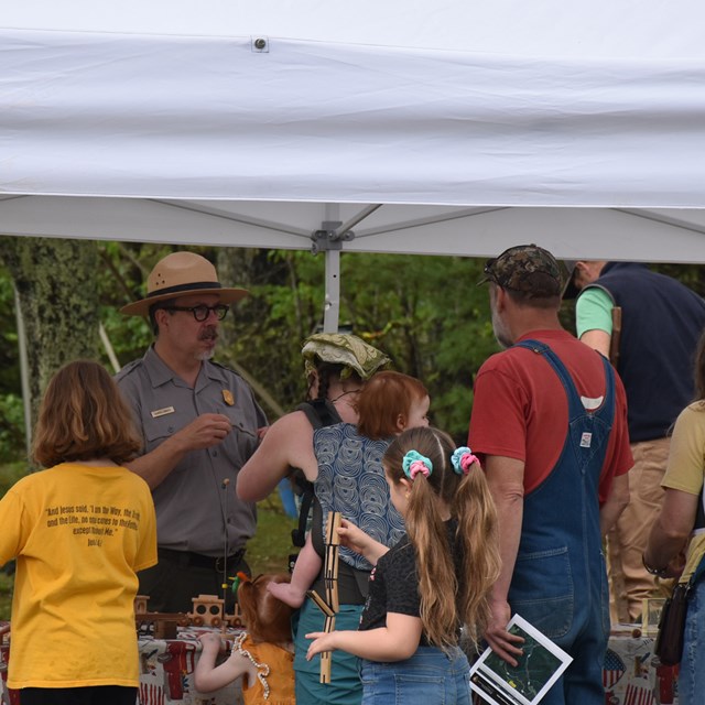 A group of people standing outside of an old timey toy tent. 