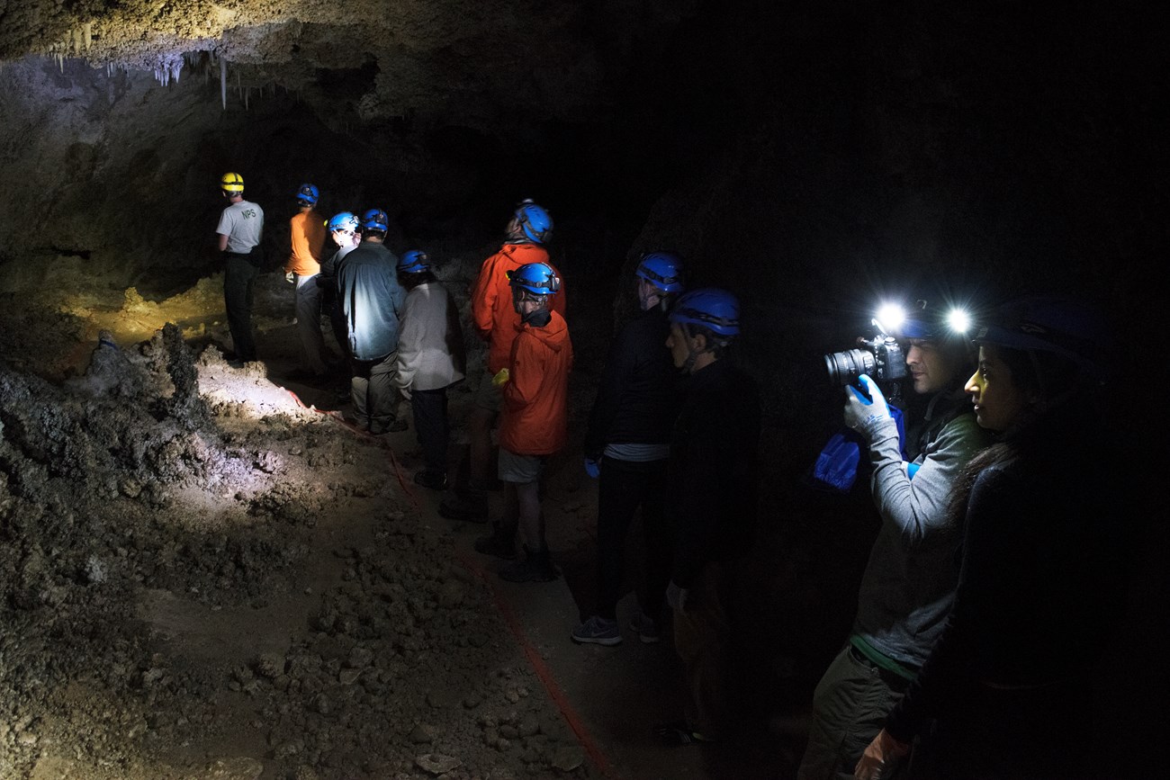 a picture of two rangers and visitors in lower cave with headlamps that illuminate cave formations