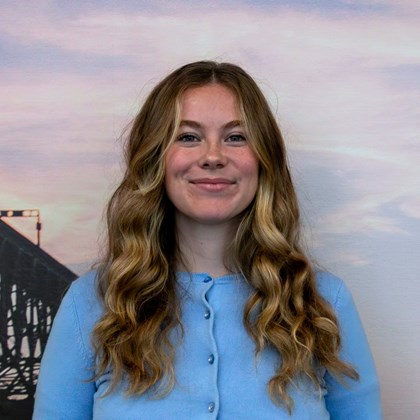 Headshot Photo of Isabella Bartels with a bridge and clouded sky background.