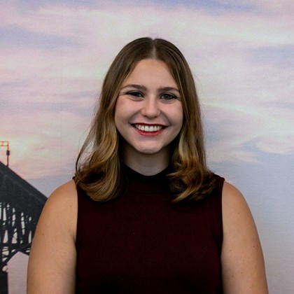 Headshot Photo of Charlotte Vaughn with a bridge and clouded sky background.
