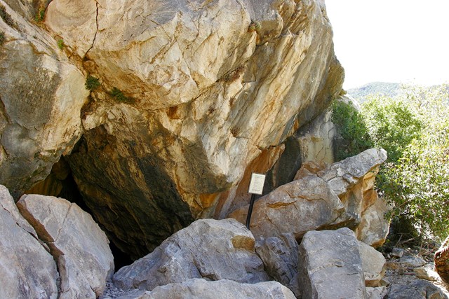 cave entrance surrounded by large rocks with trees and small sign