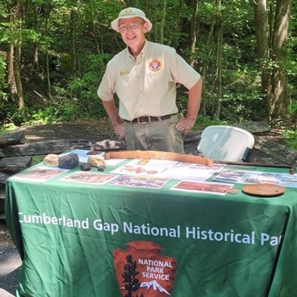 Male National Park Service volunteer standing behind a table with Furnace Friday information.