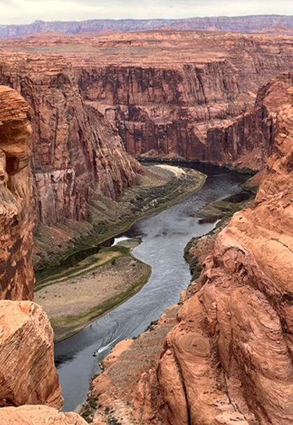 A sandstone canyon with a clear river at the bottom. Gravel bars are on the edges of the riverbed. A boat drives upstream.