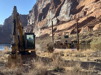 A large backhoe and a flat barge at a beach on a river