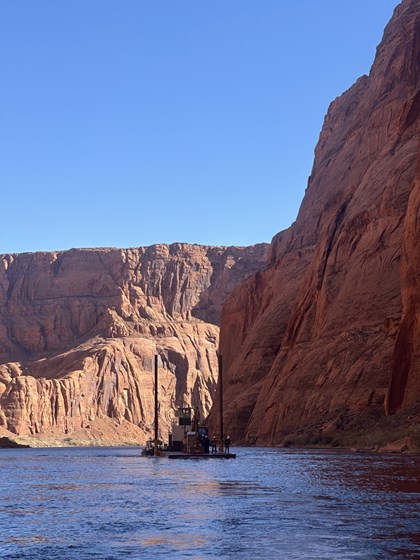 A barge with construction equipment and personnel on a river in a  scandstone canyon