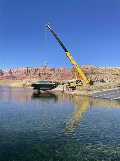 Large crane equipment holds a barge over a clear river in a sandstone canyon