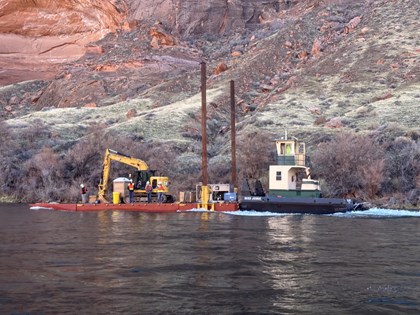 tugboat pulls a barge with construction equipment up a river