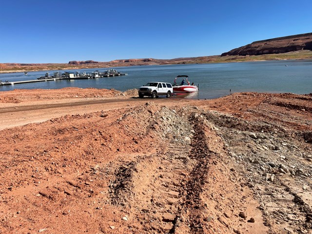 Vehicle with trailer launching a boat on a dirt ramp to a desert lake 