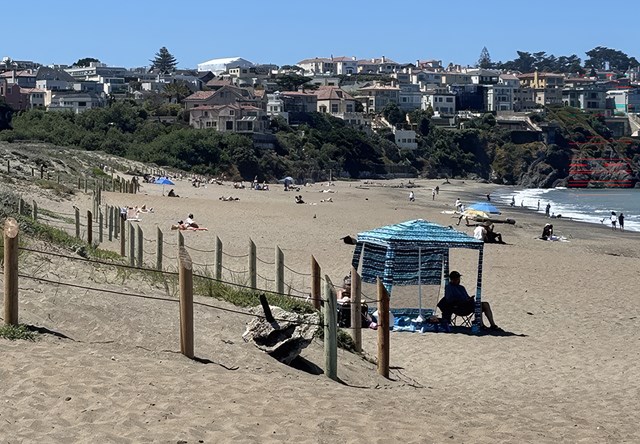 People sit on a beach with houses behind.