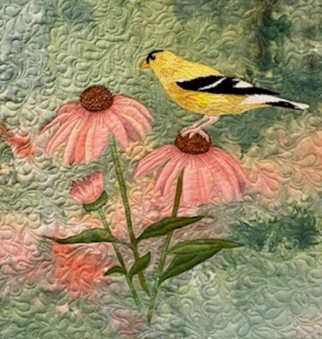 A quilt with pink flowers, a goldfinch bird, and a green backdrop.