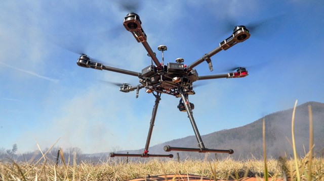 A drone taking flight in a field with a blue sky and mountain in the background.