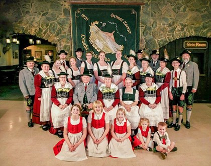 Around 30 men, women, and children are dressed traditional Germen outfits of green, red, white, and gray.