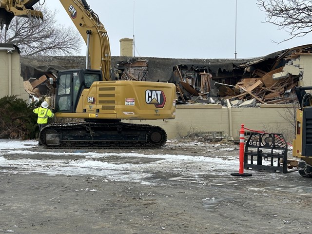 A large construction machine tears into a buildilng wall. 