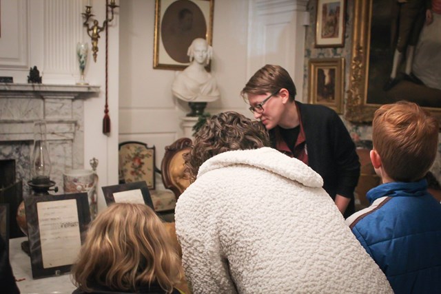 Family and staff member in a Victorian parlor looking at historic letters