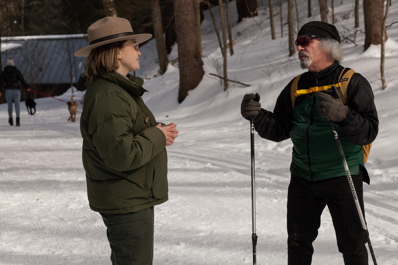Park Ranger in winter uniform talks to a cross-country skier on a snowy trail