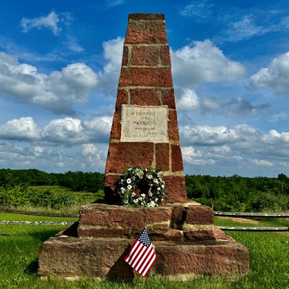 A modern image of the Groveton Monument with US flag and flower wreath.